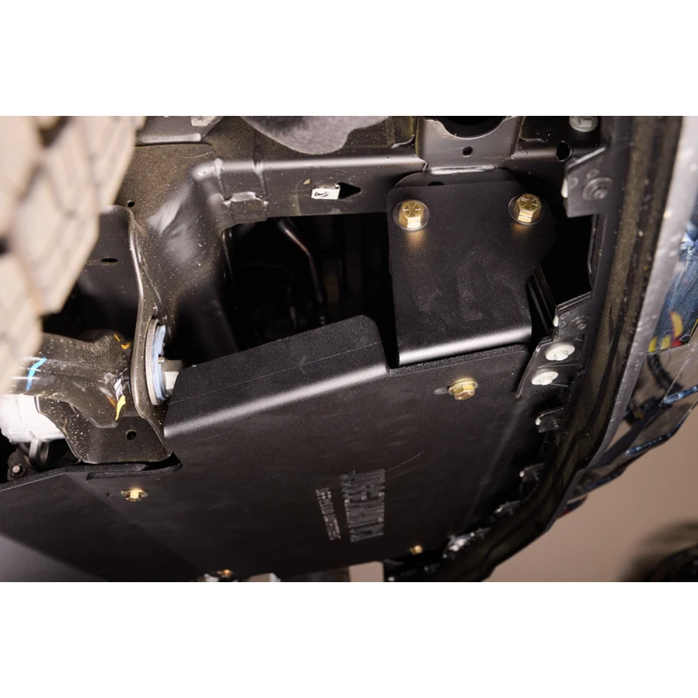 A close-up of a black metal undercarriage shield or splash panel secured with gold-toned bolts on a vehicle's chassis.