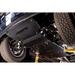 Black steel undercarriage shield and skid plate installed on a vehicle, with visible suspension, tires, and yellow support jacks in a workshop setting.