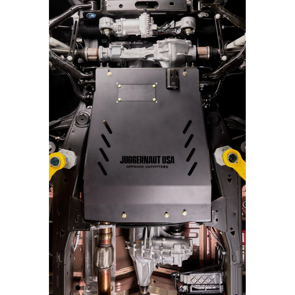 A black metal undercarriage cover with the text 'JUGGERNAUT USA OFFROAD OUTFITTERS' mounted over a vehicle's transmission and differential area, shown in a detailed undercarriage view.