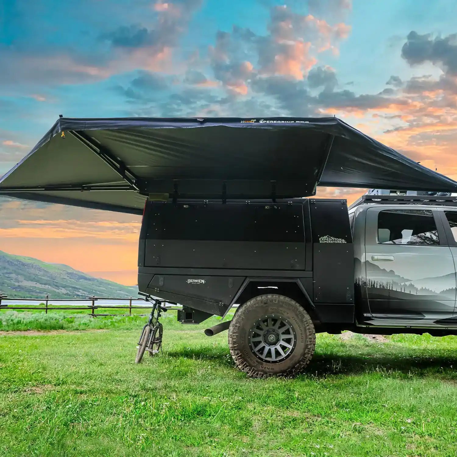Black off-road vehicle with a large 23zero 270 awning in a grassy field during sunset.
