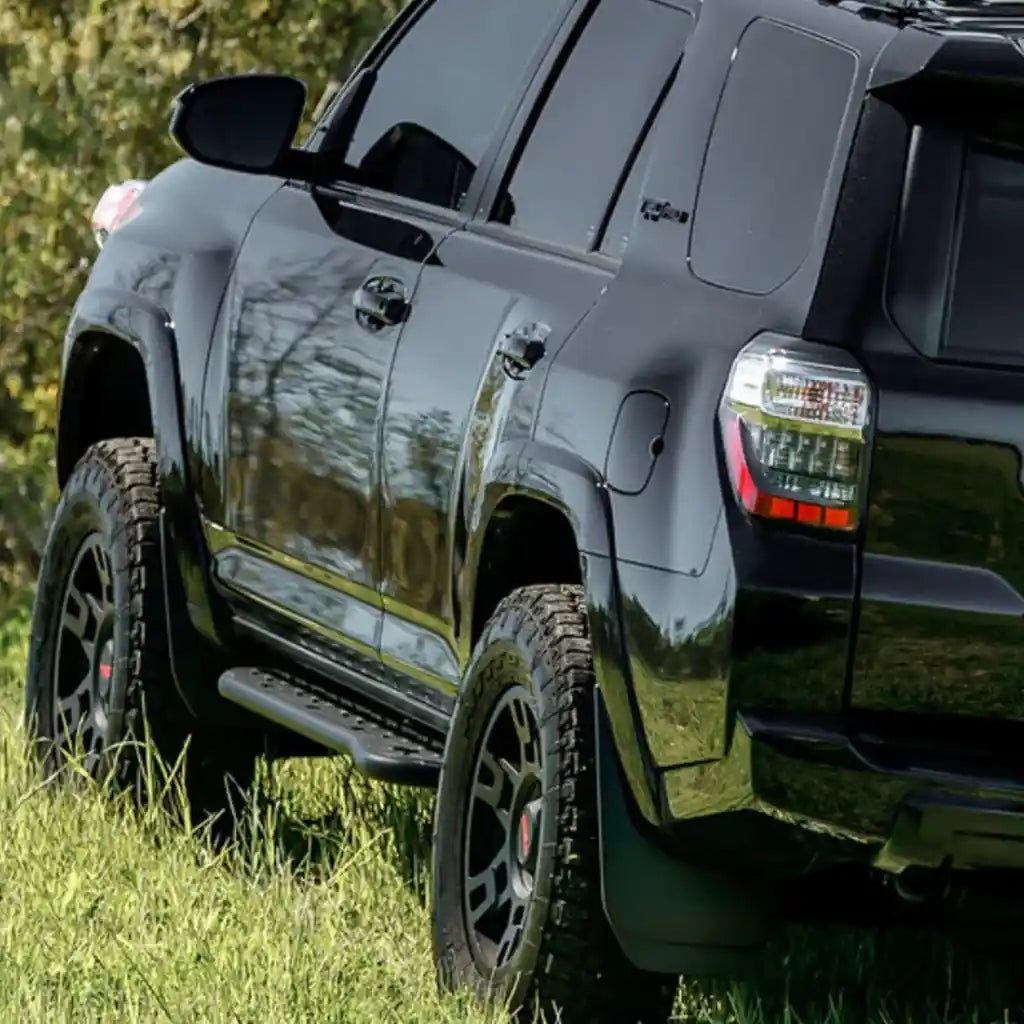 side view of Black 4runner with cali raised rock sliders parked on grass with a blurred natural background