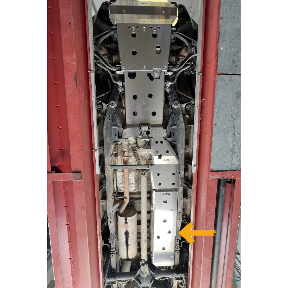 Close-up of a installed fuel tank skid plate inside a vehicle, with an arrow pointing to a specific part.