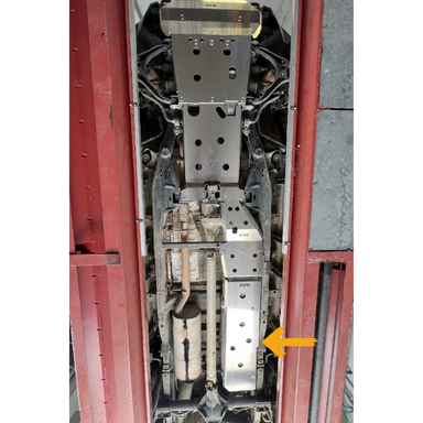 Close-up of a installed fuel tank skid plate inside a vehicle, with an arrow pointing to a specific part.