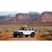 White Jeep Wrangler with mounted roof rack on a dirt road with desert landscape and mountains in the background