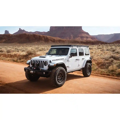 White Jeep Wrangler Rubicon with mounted Starlight roof rack on a desert road with desert landscape in the background