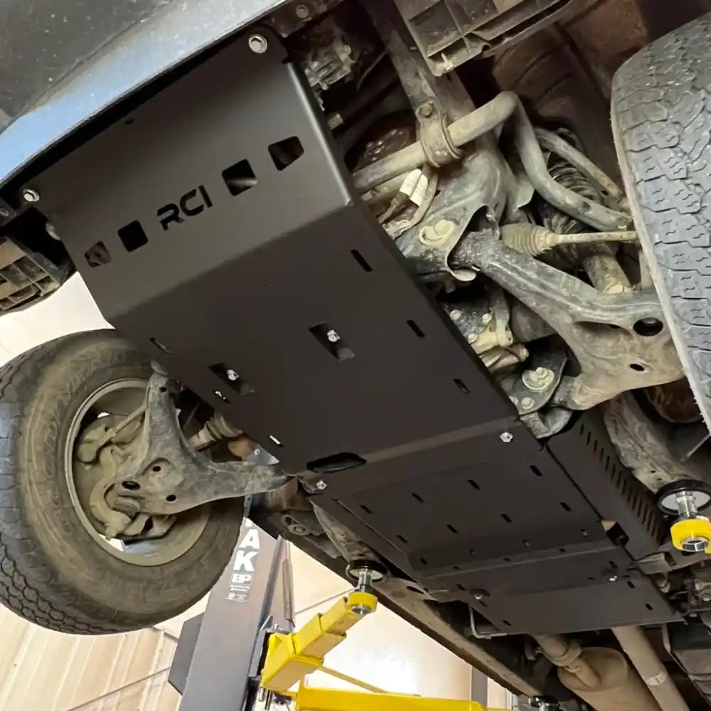 Black RCI front differential or engine skid plate installed on Colorado undercarriage, angled view near wheel