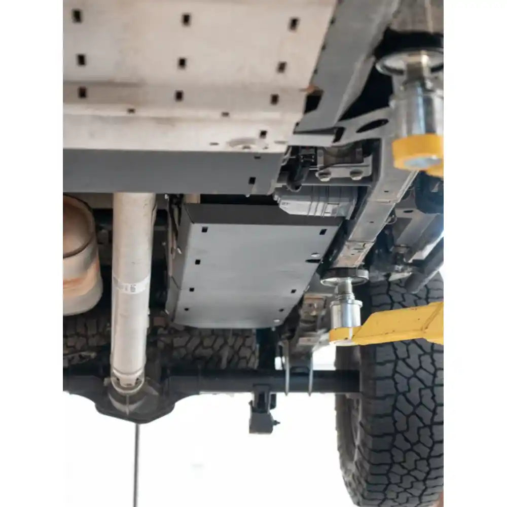 Black RCI fuel tank guard bolted in place under truck chassis, mid-rear perspective