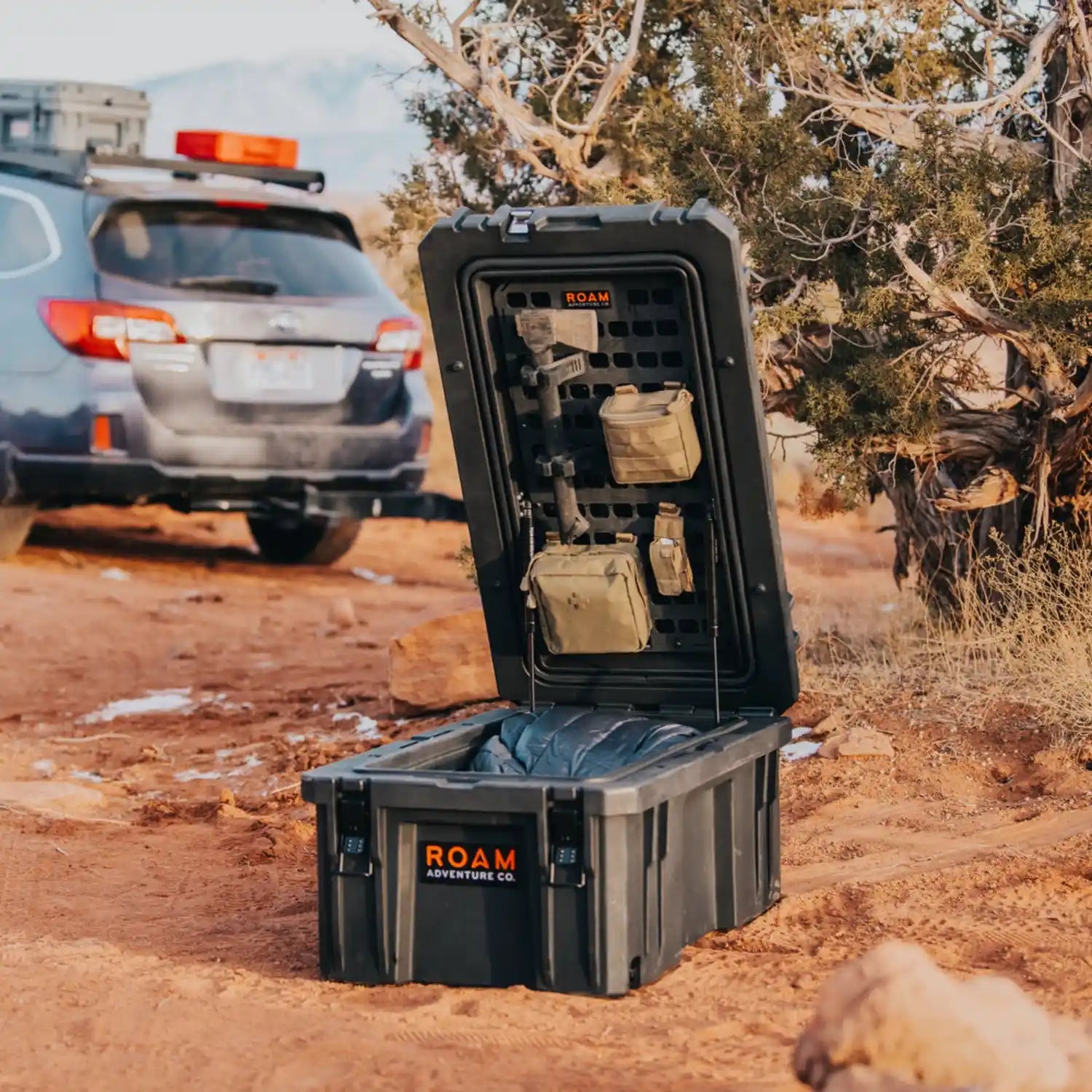 Black storage box with 'ROAM' branding on a dirt road with a vehicle in the background.