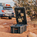 Black storage box with 'ROAM' branding on a dirt road with a vehicle in the background.