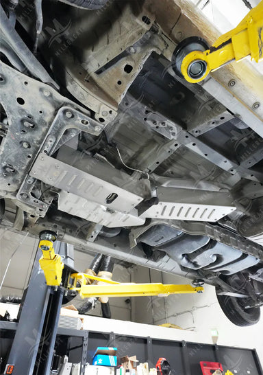 Close-up of a vehicle undercarriage with yellow mechanical arms in a workshop setting.
