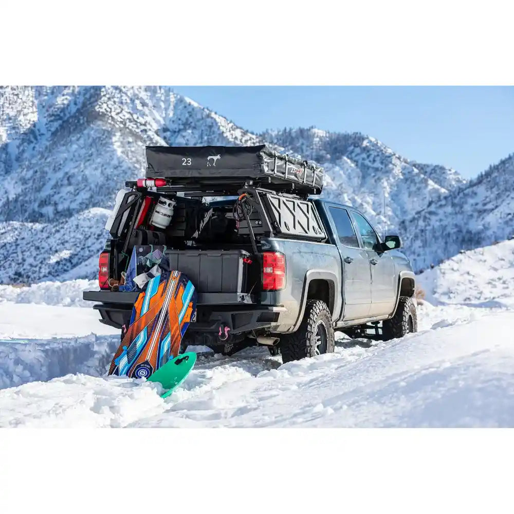 Chevy with mounted ACS bed rack by Leitner and snowboard gear in a snowy mountain landscape