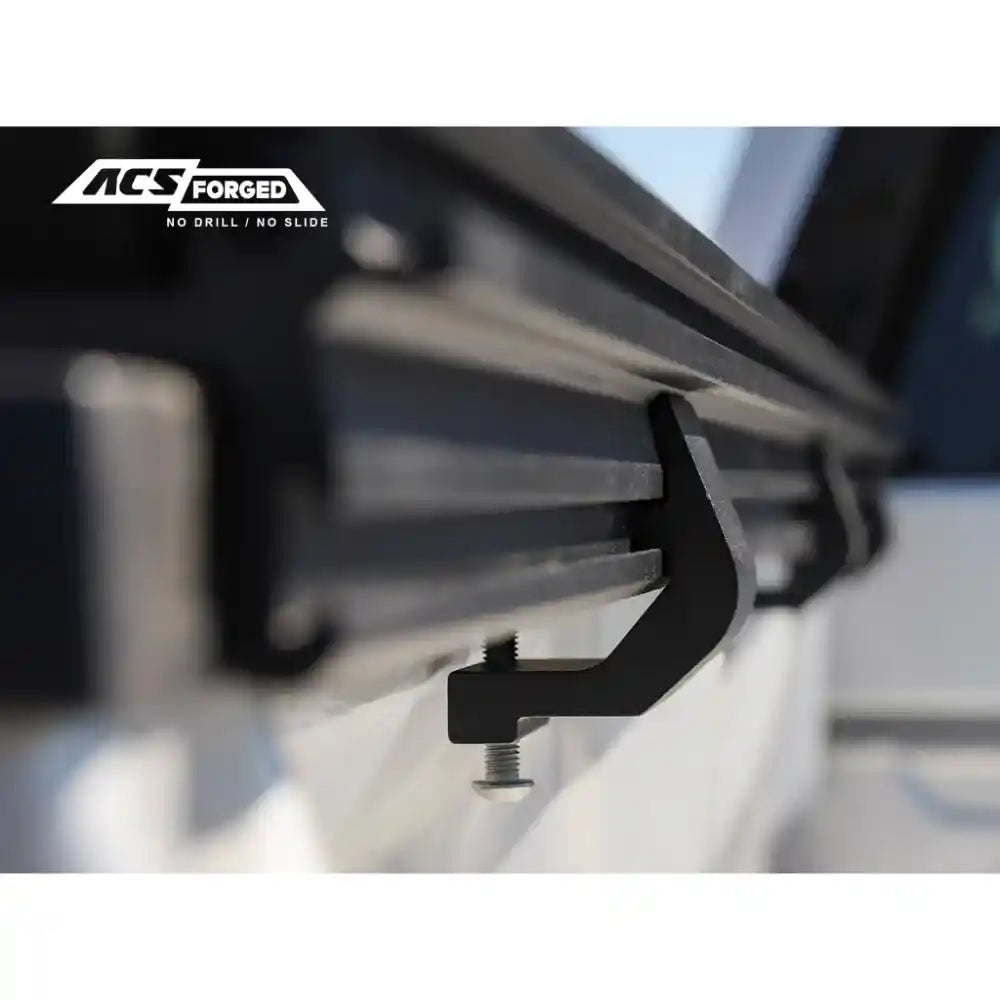 Close-up of a black metal bed rack bracket with 'ACF Forged' branding on a blurred background.