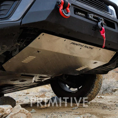 Close-up of a vehicle's undercarriage skid plates with 'Primitive Racing' branding on a rocky terrain.