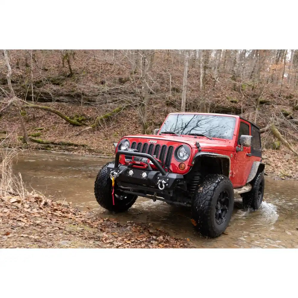 Warrior Stealth Winch Mounted on Red Jeep Wrangler driving through a shallow stream in a forest