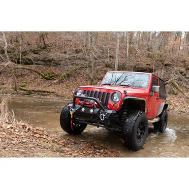 Warrior Stealth Winch Mounted on Red Jeep Wrangler driving through a shallow stream in a forest