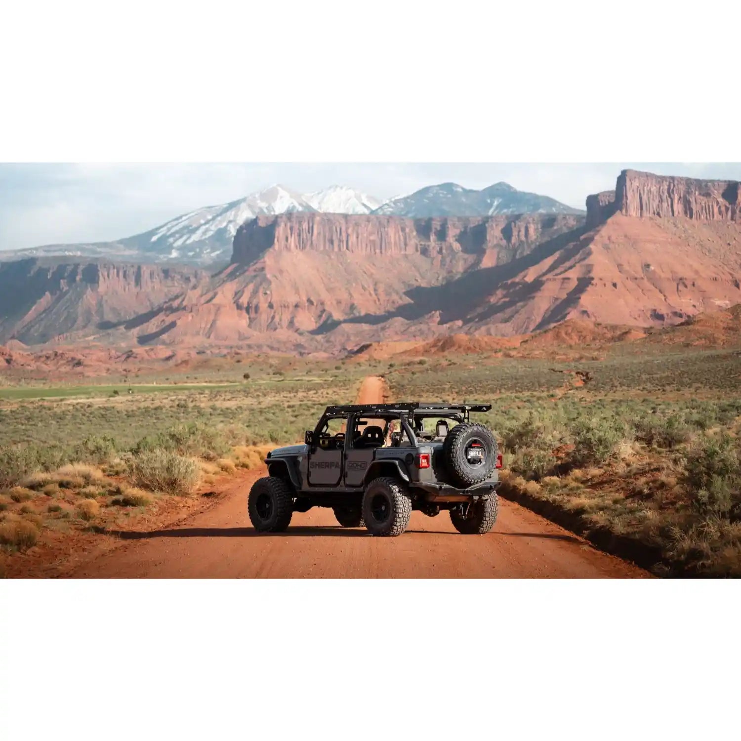 Jeep with no roof and mounted roof rack on a dirt road with desert mountains in the background
