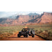 Jeep with no roof and mounted roof rack on a dirt road with desert mountains in the background