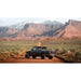 Black off-road gladiator with mounted QDHD Sherpa roof rack on a dirt road with red rock formations and snow-capped mountains in the background.
