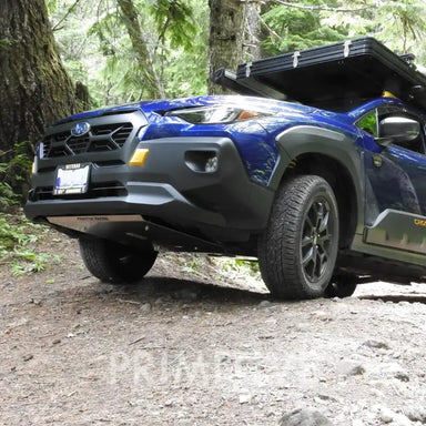 Blue Crosstrek with mounted front skid plate and with a roof rack parked on a dirt path in a forest