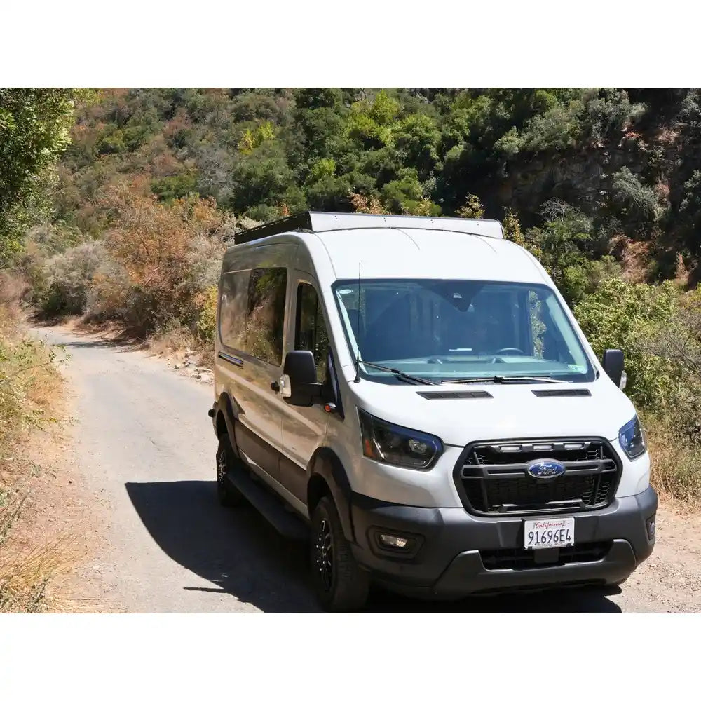 Ford van with roof rack on a scenic road with trees in the background
