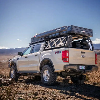 Ford truck with a bed rack and cargo box in a desert landscape.
