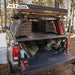 GMC bed with a tonneau cover and ACS Bed Rack, including a cooler and tools, in a forest setting.