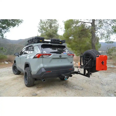 Gray RAV4 with swing out tire carrier and a red toolbox attached, parked outdoors with trees in the background.