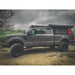 Gray SuperDuty truck with a black roof rack and bed cover on a dirt road with trees and cloudy sky in the background.