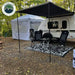 Small trailer with an awning and outdoor furniture in a wooded area, featuring Overland Vehicle Systems logo.
