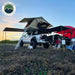 Truck with rooftop tent and overlanding equipment in a field, featuring Overland Vehicle Systems logo.