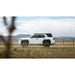 White 4Runner with mounted roof rack parked on a dirt road with mountains in the background