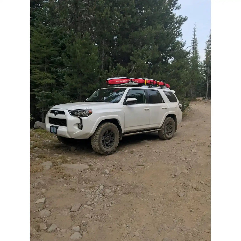 White SUV with rock sliders on a dirt road surrounded by trees