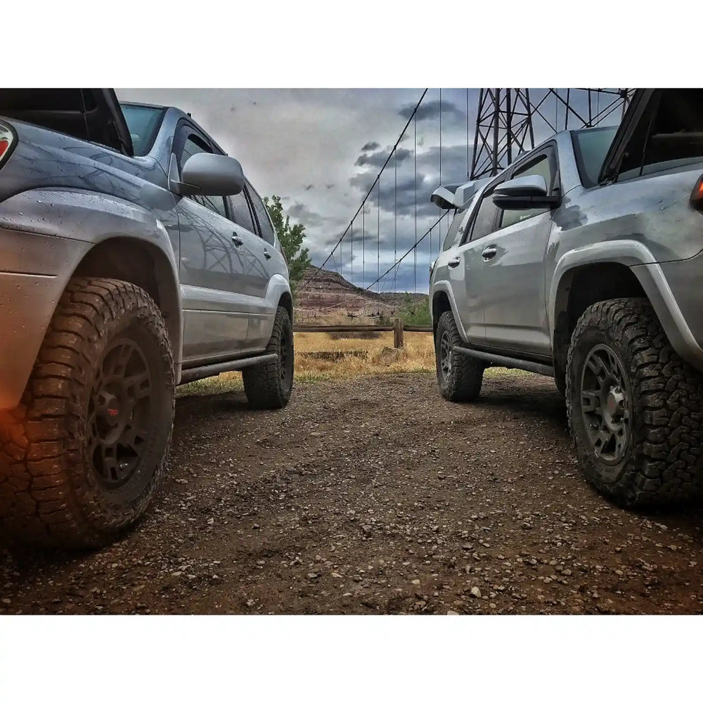 Two off-road vehicles on a dirt road with a mountainous landscape in the background.