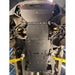 Black underbody shield and skid plate kit installed on a vehicle chassis, with yellow jack stands supporting the vehicle in a garage setting.