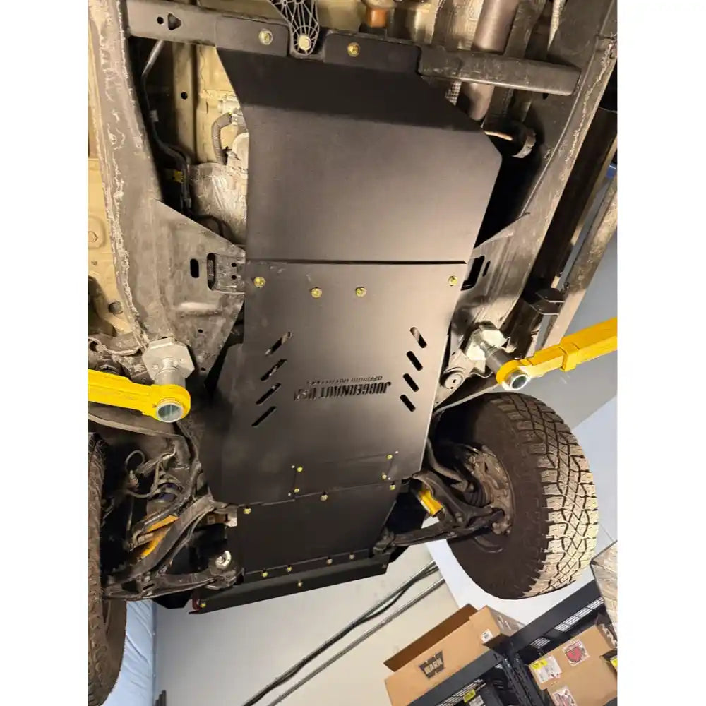 A black metal undercarriage shield with the brand name 'JUGhead' printed on it, installed on a vehicle lift in a garage.