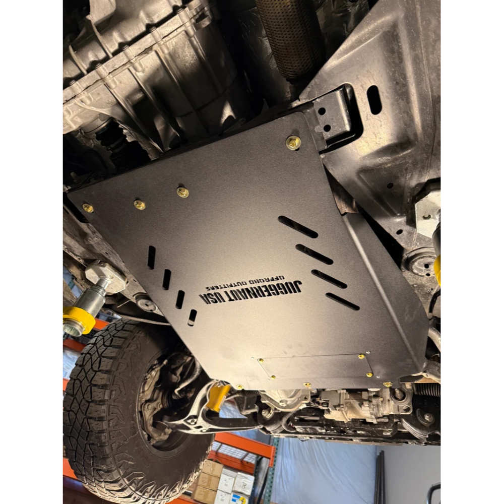 A black metal undercarriage shield with the text 'JUGGERNAUT USA' and 'ENGINEERED OUTSIDE' printed on it, installed on a vehicle undercarriage.