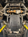 A black steel underbody shield with the text 'Jubereen Auto' printed on it, installed on the bottom of a vehicle. The vehicle is shown underneath on a lift, with yellow wheel chocks visible on both sides.