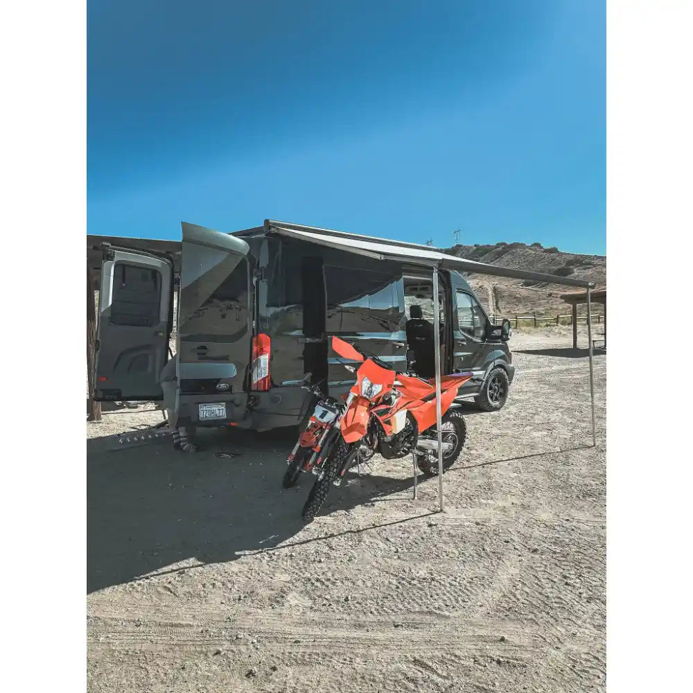 Van with open doors and a red dirt bike on a dirt road under a clear blue sky.
