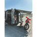 Van with open doors, a motorcycle, and an awning in a desert-like setting