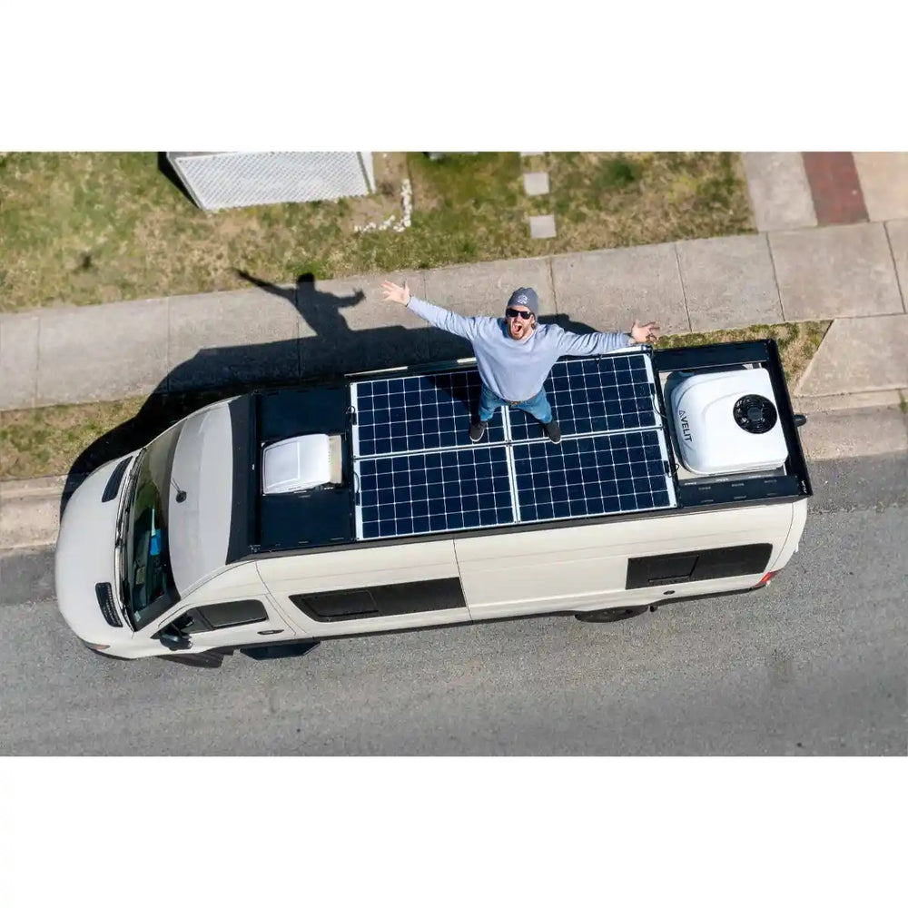 Man standing on a van with solar panels on its roof, on a street.