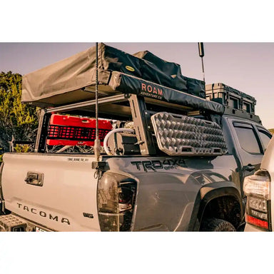 Off-road vehicle with a roof tent and Cali Raised Bed Rack in a natural setting.