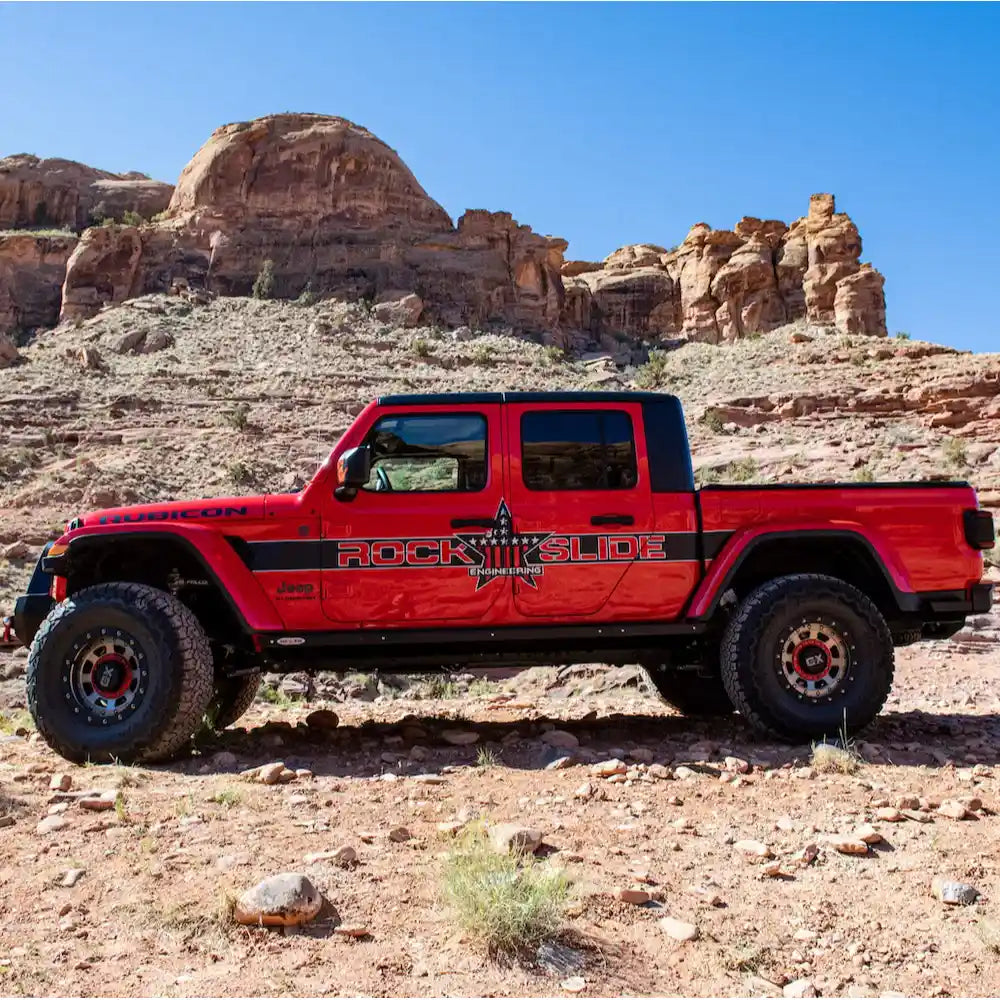 Orange Jeep Gladiator JT off-road on rocky desert terrain with rock sliders
