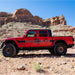 Orange Jeep Gladiator JT off-road on rocky desert terrain with rock sliders