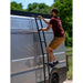 Man climbing a ladder on the side of a van with trees in the background