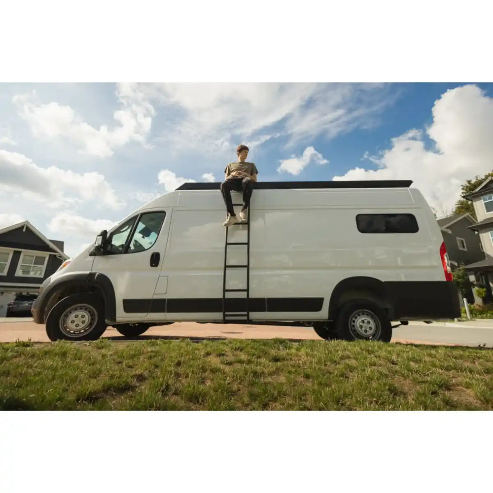 Person sitting on top of a white van with a ladder, under a blue sky with clouds.