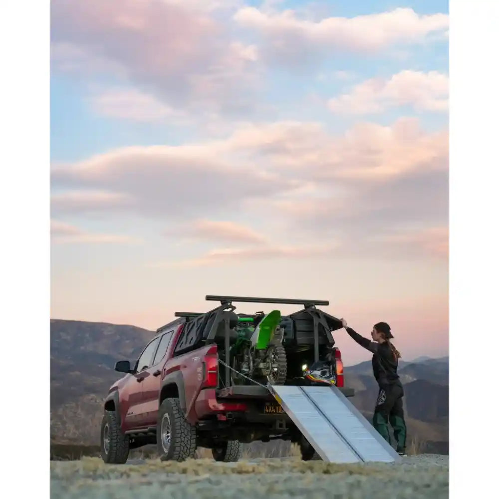 Person loading motorbike on Tacoma with installed ACS FORGED Bed Rack on Toyota