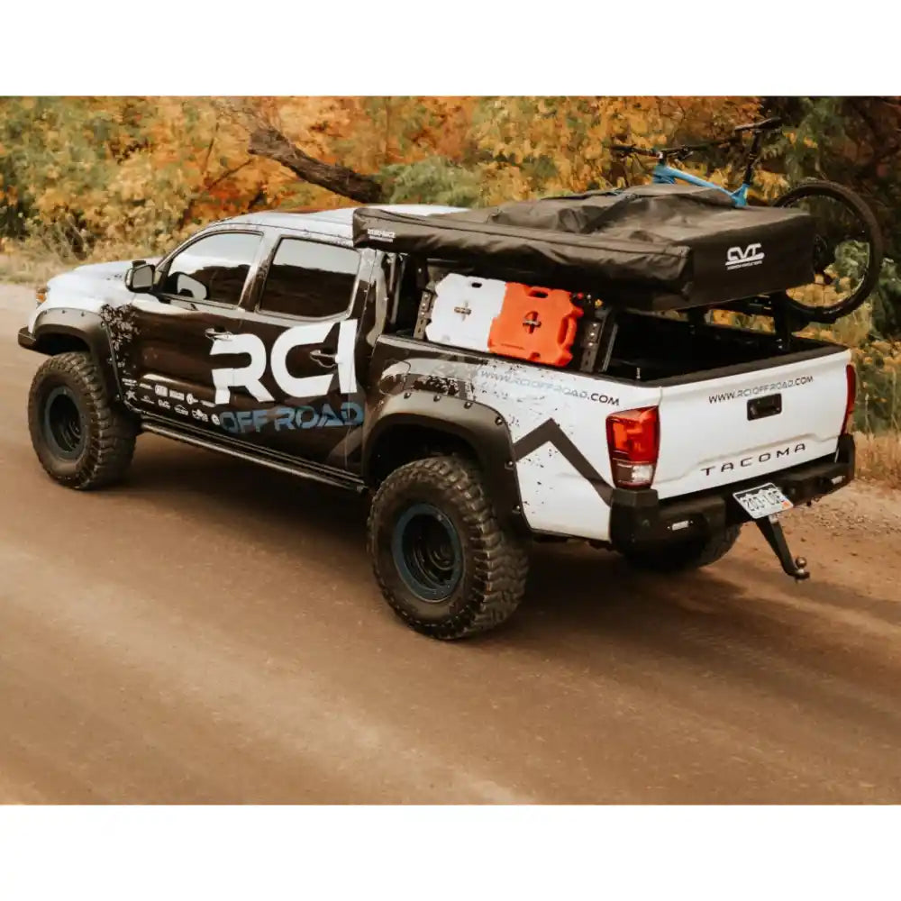 RCI Offroad Tacoma with HD bed rack loaded with bike and rooftop tent on dirt road