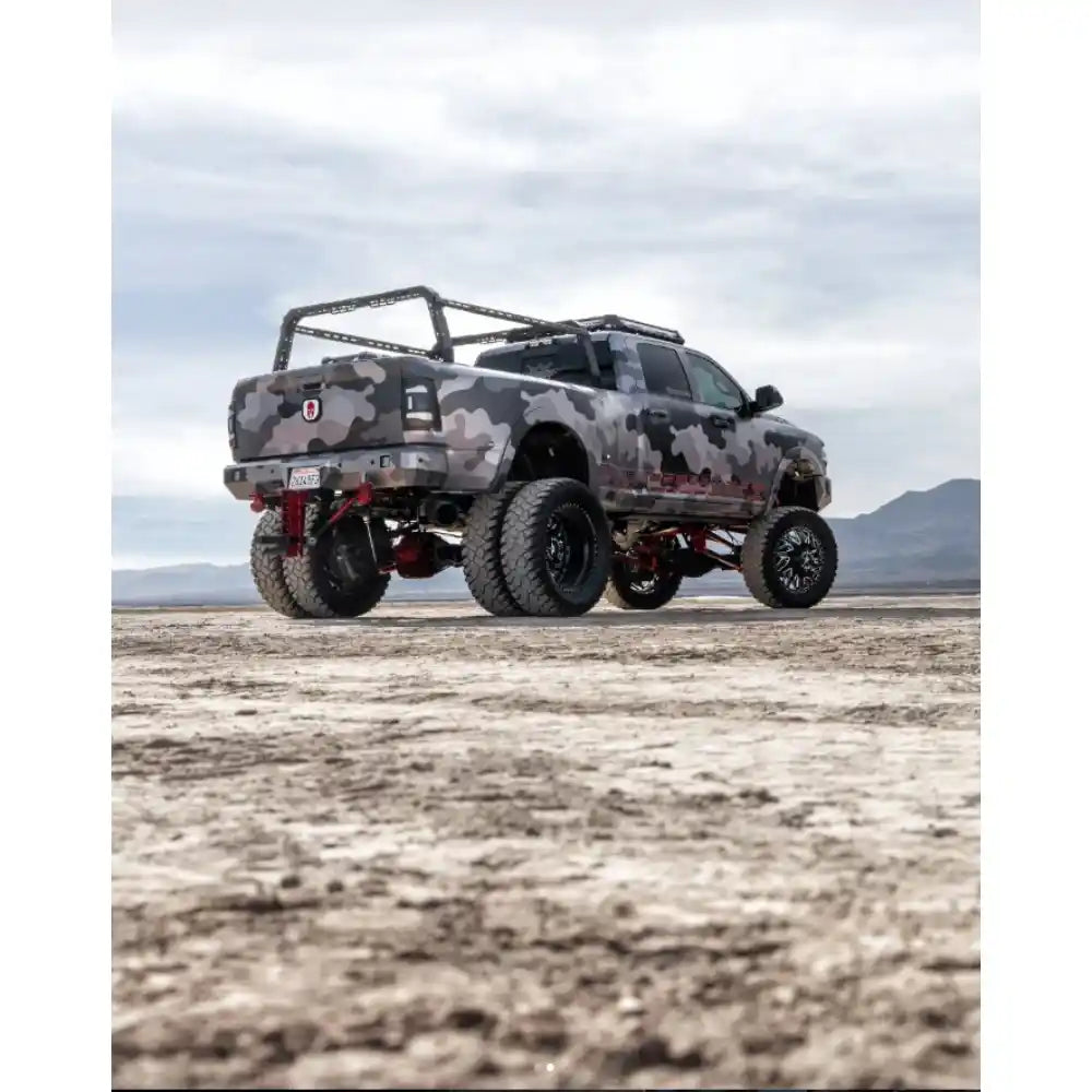 Camouflage-patterned RAM truck with mounted bed rack on a barren landscape with mountains in the background