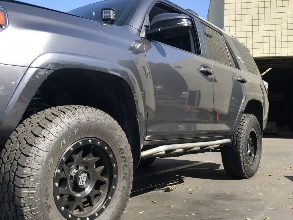 Black SUV with large off-road tires and trail rock sliders visible branding on a paved surface.
