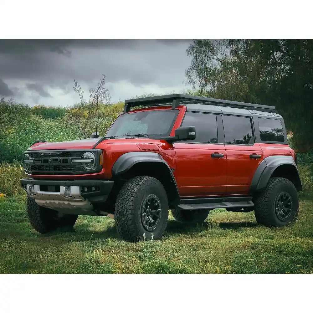 Red Bronco with a black Letiner Designs roof rack on a grassy field with trees in the background